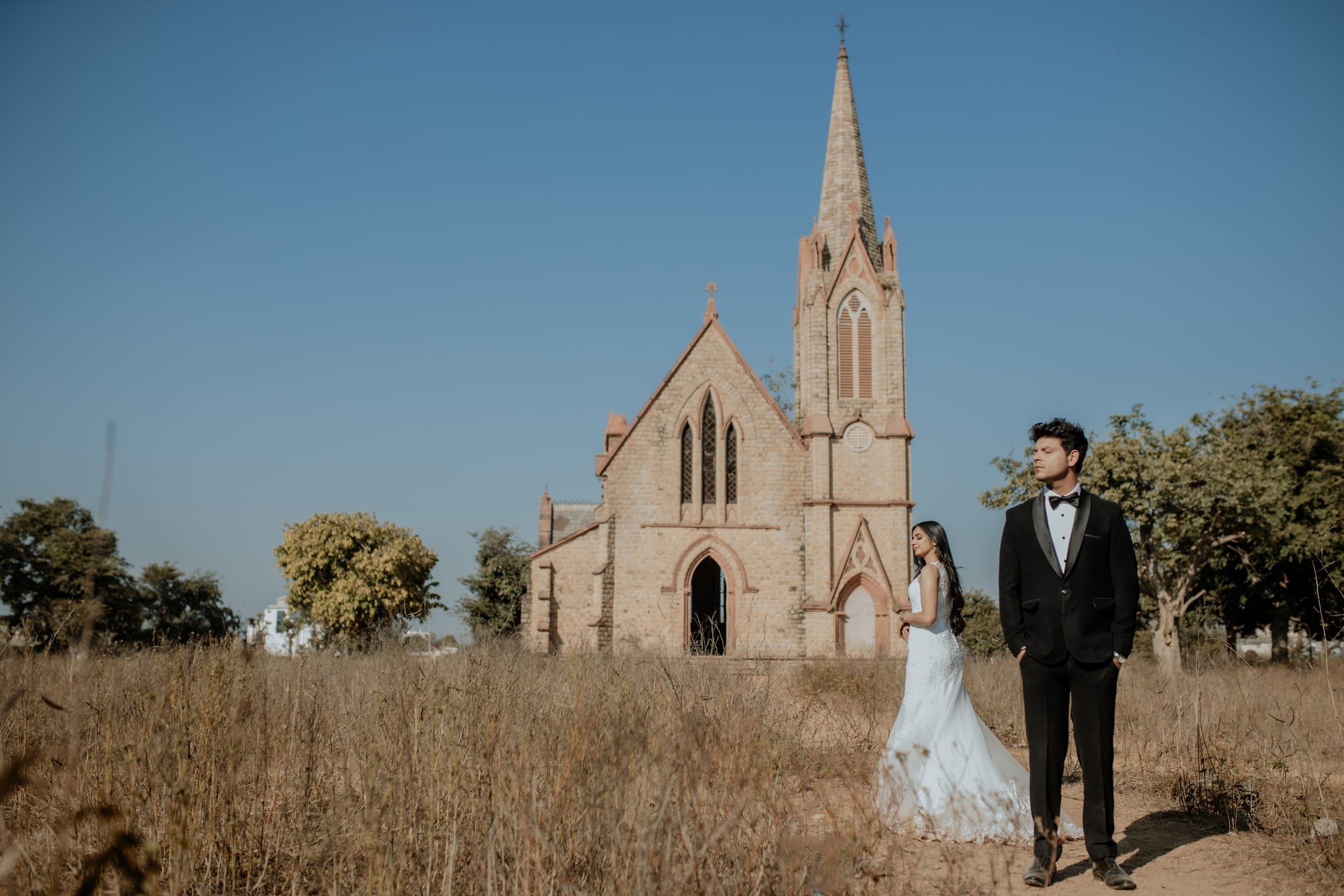 Bride and groom before a church spire in an open Goan field